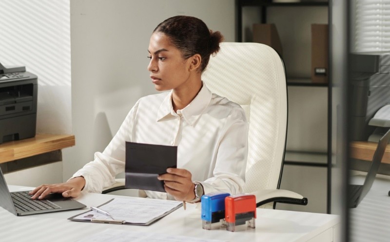 business student at a desk with computer, papers, and stamps